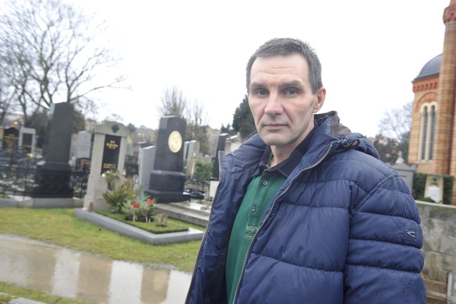 Ein ernst dreinblickender Mann mit T-Shirt und Jacke steht auf dem Friedhofsgelände