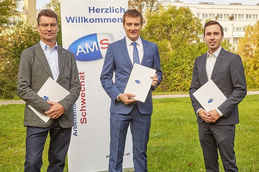 Drei Männer in Anzügen vor einem Schild des AMS Niederösterreich