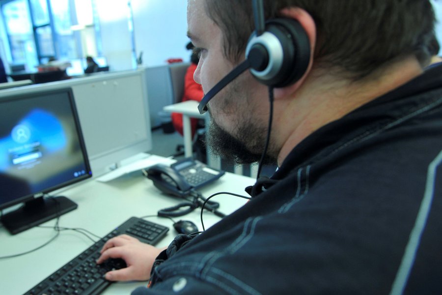 Ein Mann mit dunklem Haar und Bart, ausgerüstet mit Headset,  an seinem Call-Center-Arbeitsplatz. ausgerüstet mit Headset