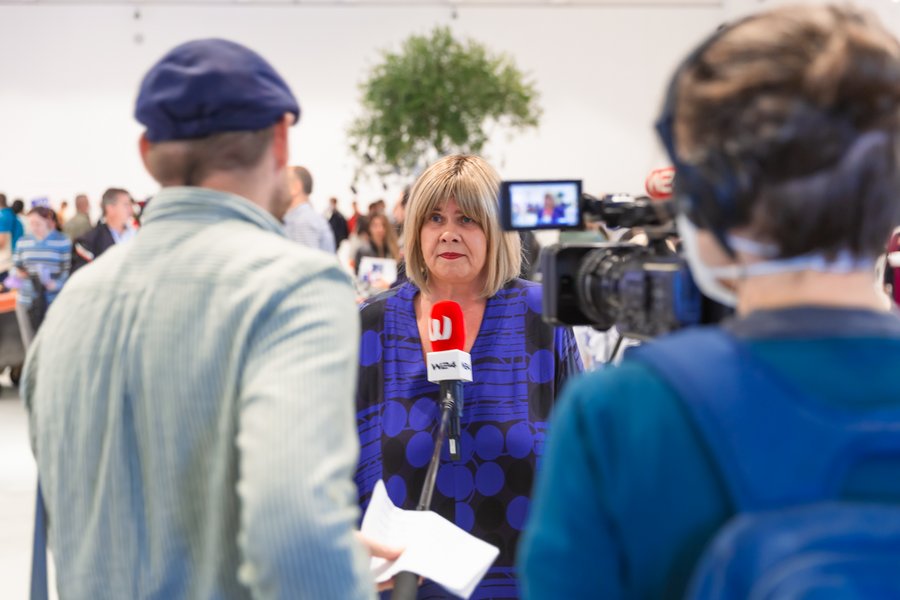 Eine Frau im blauen, gemusterten Kleid wir von einem Fernsehsender interviewt.