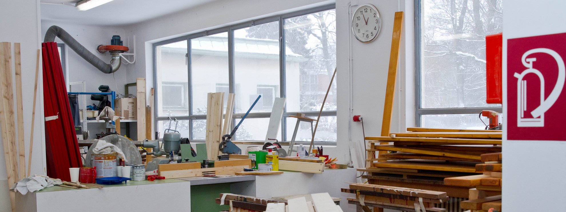 Blick in eine Werkstatt mit Holzbrettern, Farbtiegeln und Schneidemaschine