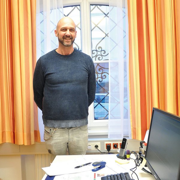 Wilfried Schagl, ein Mann mittleren Alters mit Glatze und Vollbart steht an seinem Schreibtisch