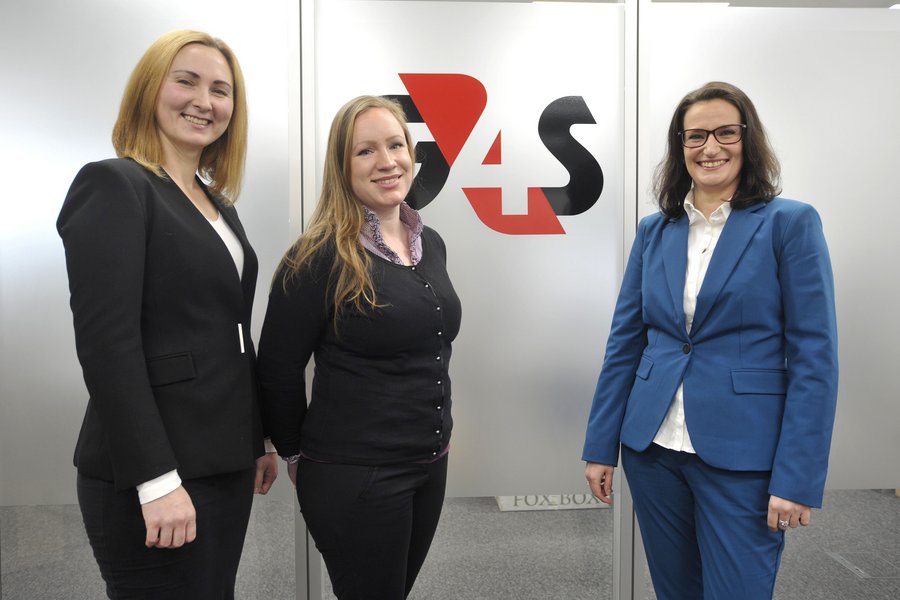 Drei junge Frauen im Business-Outfit vor dem Logo der Firma G4S
